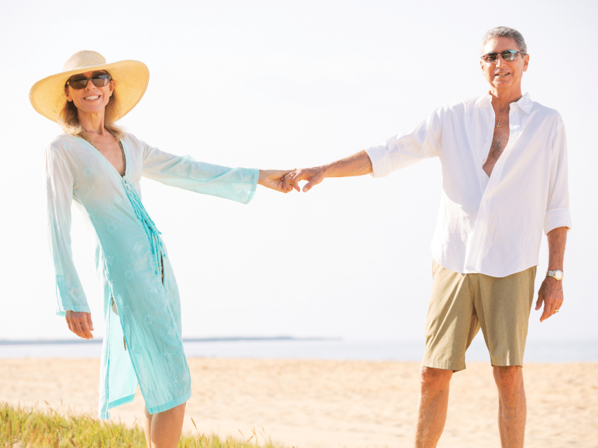 couple après 50 ans souriant en tenue décontractée se donnant la main sur une plage